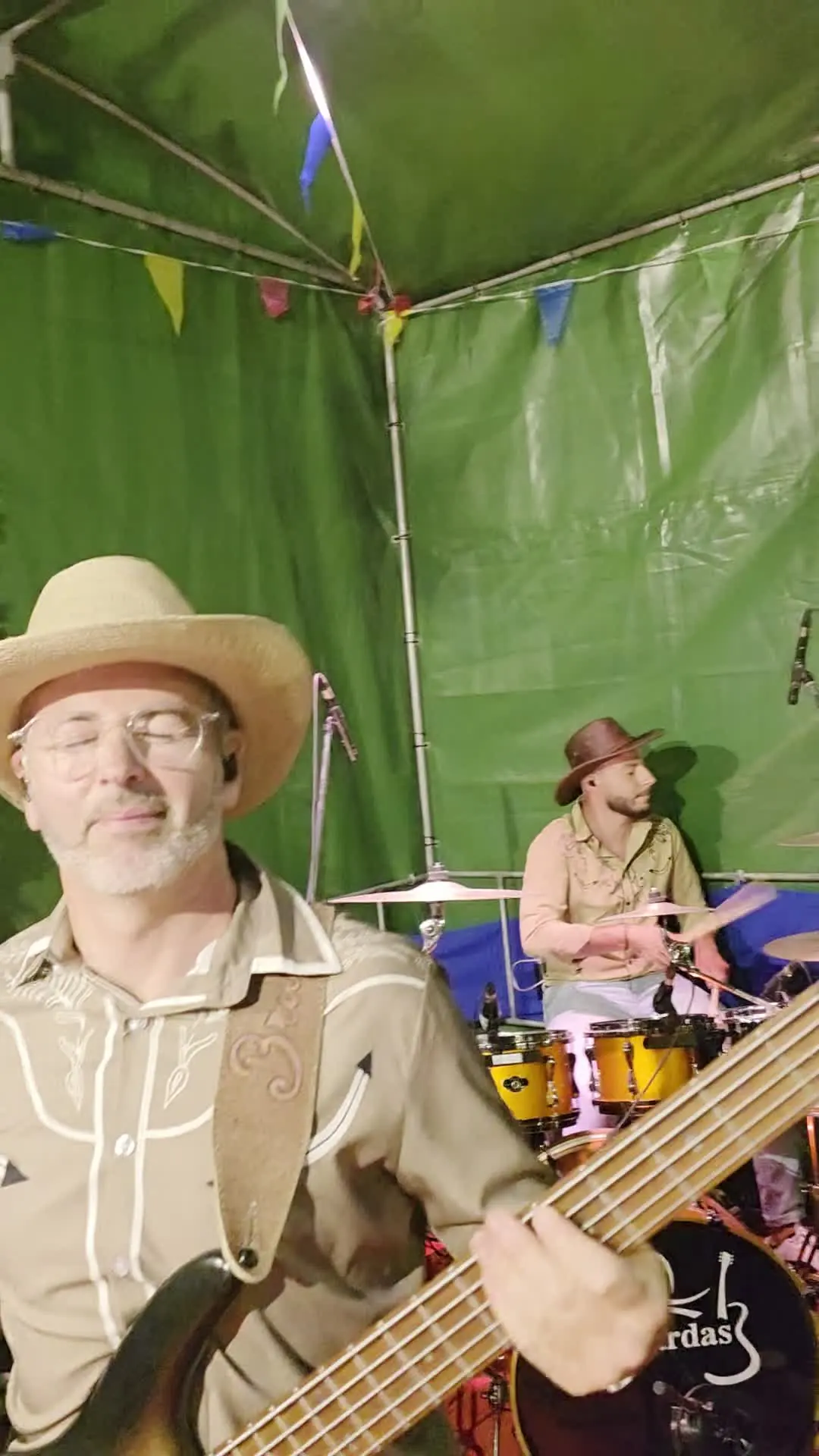 Músicos no palco com chapéus de cowboy, baixo e bateria.